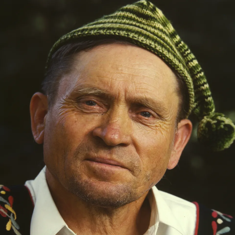 Kodachrome portrait of a weathered, smiling man in a striped knitted cap and an embroidered vest