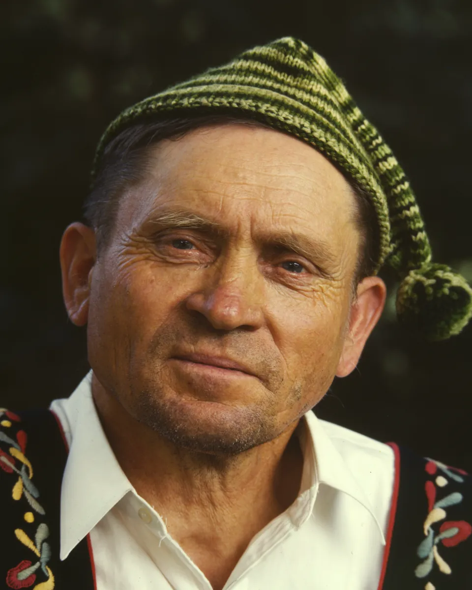 Kodachrome portrait of a weathered, smiling man in a striped knitted cap and an embroidered vest